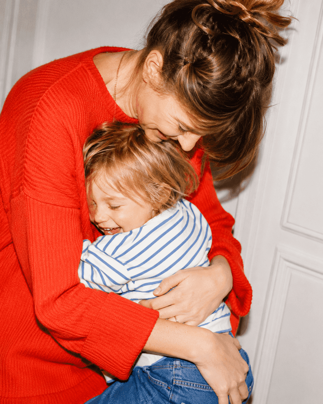 Mama w czerwonym swetrze przytula uśmiechnięte dziecko