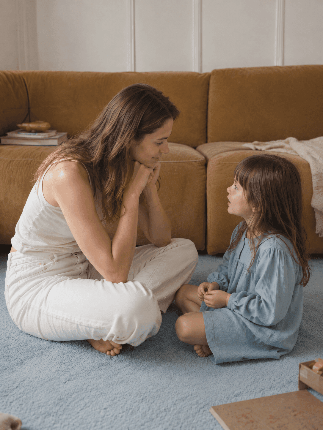 Mama rozmawia z córką siedząc z nią na dywanie